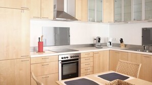 A modern kitchen with wooden cabinets, a stainless steel range hood, a built-in oven, a coffee maker, and a sink. - Holiday Apartment Faller-greiner (Bad Bergzabern)