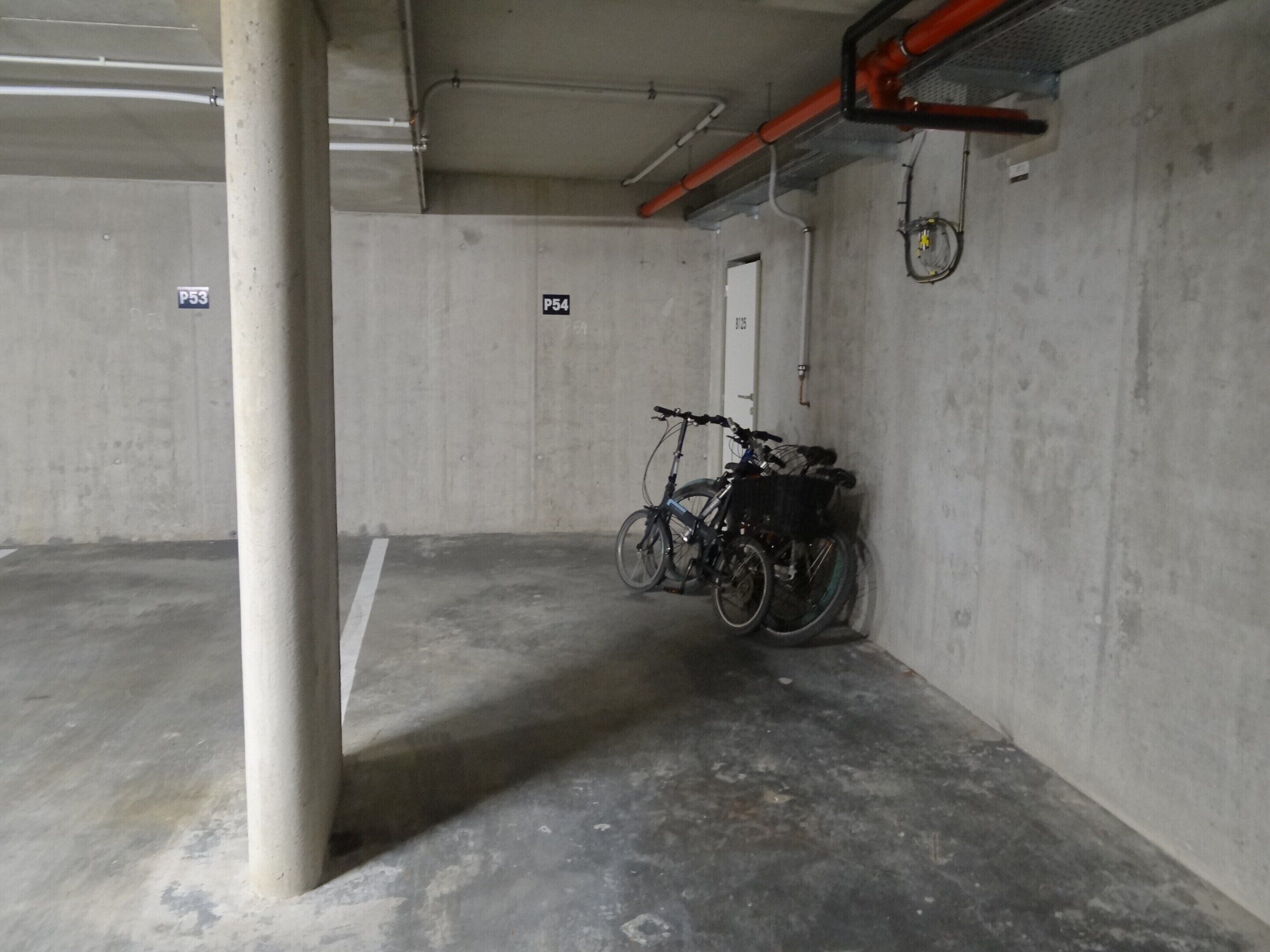 Un garaje de estacionamiento con paredes de concreto, un pilar blanco y una bicicleta apoyada en la pared.