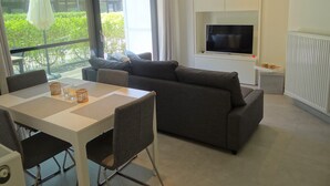 A modern living room with a sofa, dining table, and TV. - Apartment Nieuwpoort Near Beach (Nieuwpoort)