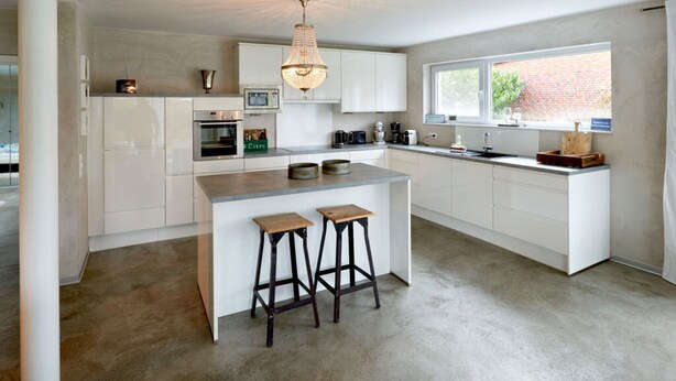 Una cucina moderna con mobili bianchi, un'isola centrale con sgabelli, un lampadario e una finestra che lascia entrare luce naturale.