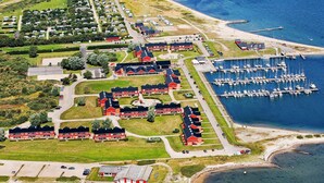 Luchtbeeld van een kustgebied met woonhuizen, meerdere gebouwen met rode daken, een jachthaven vol boten en een weg naar het strand.