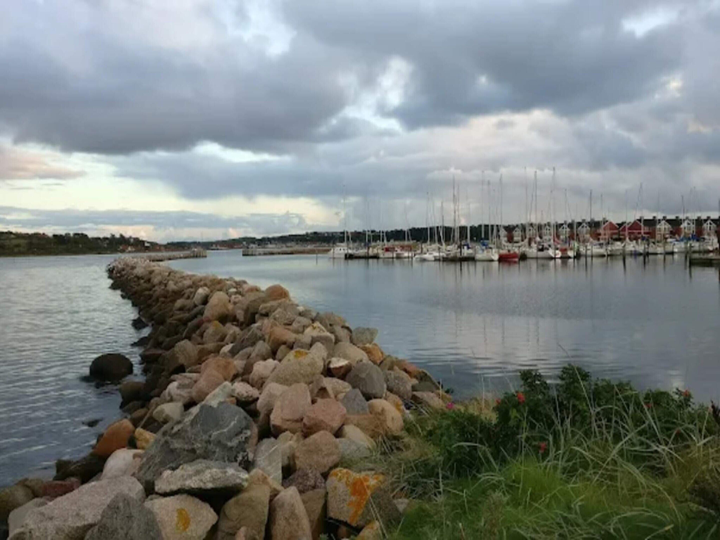A marina with boats docked, a rocky breakwater, and a calm water body.