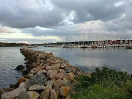 A marina with boats docked, a rocky breakwater, and a calm water body.