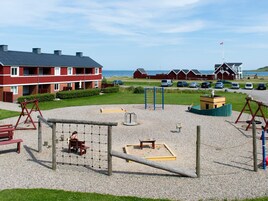 A playground with various play equipment, a bench, and a building with a red facade in the background.
