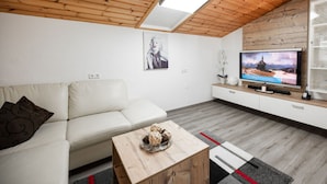 A modern living room with a wooden ceiling, a white sofa, a coffee table, a flat-screen TV, and a decorative plant. - Present Apartment in Fusch (Fusch an der Grossglocknerstrasse)