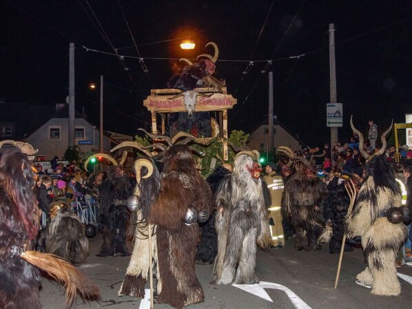Evento nocturno al aire libre con participantes vestidos con trajes típicos y un carro alegórico decorado.