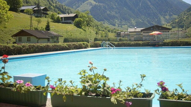 A swimming pool with a mountain backdrop, surrounded by houses and potted plants. - Present Apartment in Fusch (Fusch an der Grossglocknerstrasse)
