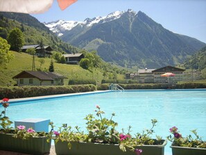 Piscina con montañas al fondo, rodeada de casas y plantas en macetas.