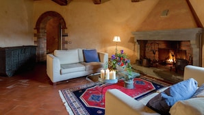 A cozy living room with a fireplace, a white sofa, a coffee table with candles, and a rug. - Villa in Cortona With Pool & Hill Views (Cortona)