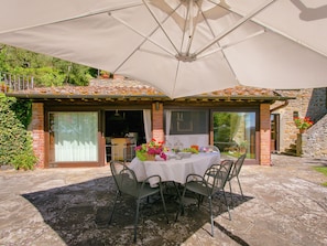 Eine Terrasse mit Esstisch und Stühlen, beschattet von einem großen Sonnenschirm.