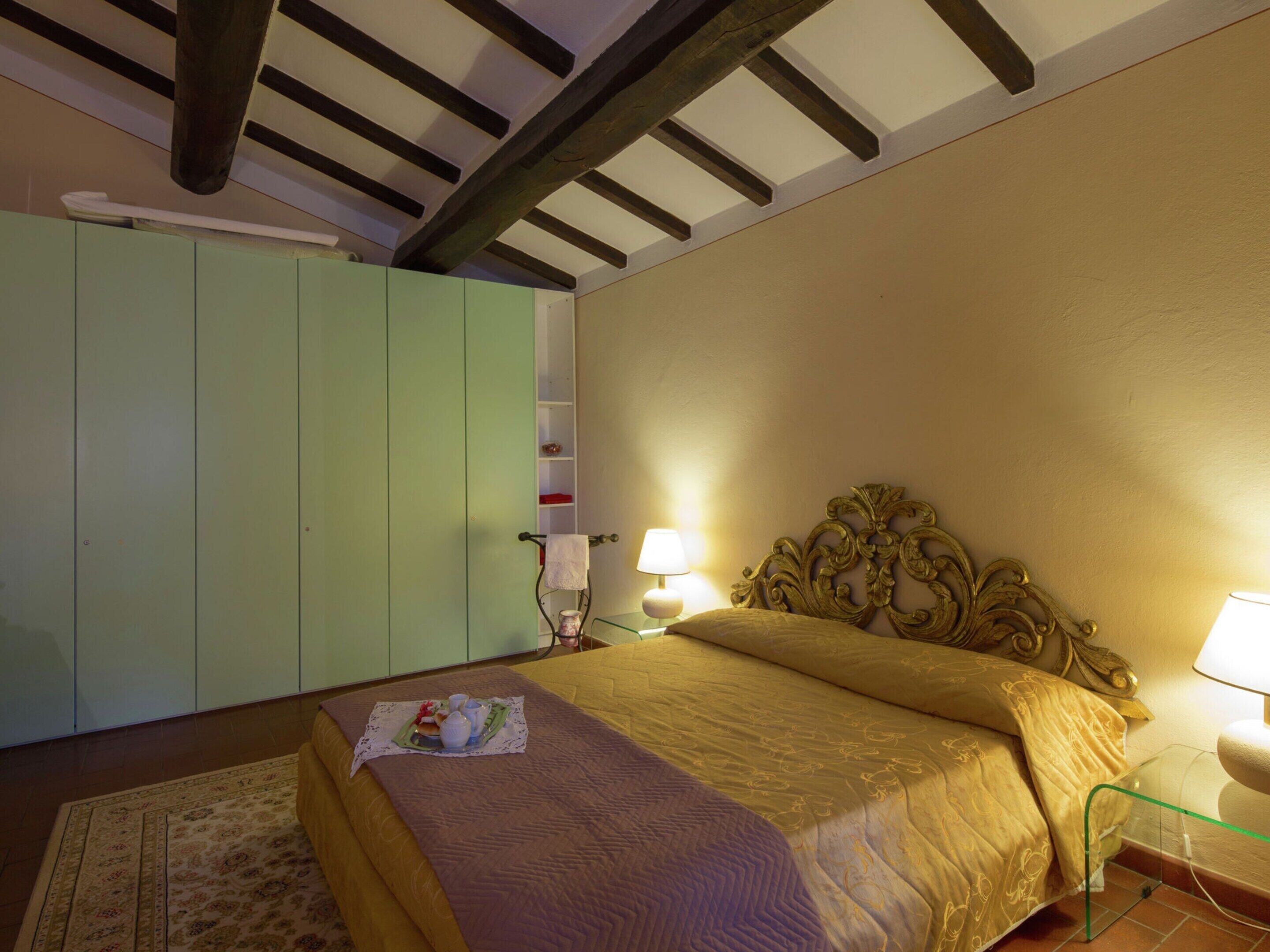 A bedroom with a bed, a nightstand, a lamp, a wardrobe, and a decorative headboard.
