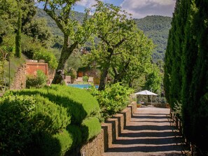 A pool area with steps leading down to a pool, surrounded by lush greenery and trees. - Villa in Cortona With Pool & Hill Views (Cortona)