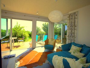 A spacious living room with a large sofa, a coffee table, and a rug. There are two chairs and a table outside the room. - Ferienhaus "marianne" in Breege (Breege)