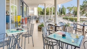 An outdoor patio area with tables and chairs, large windows, and a view of the street. - Apartment in Caorle Near the Beach (Caorle)