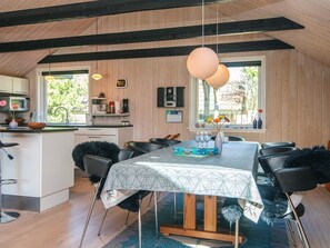 A modern kitchen with wooden paneling, a dining area with a geometric tablecloth, and a view of the outdoors through large windows. - 4 Star Holiday Home in Blavand (Blavand)