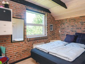 A bedroom with a brick wall, a window, a bed with white bedding, and a small dresser. - 4 Star Holiday Home in Blavand (Blavand)