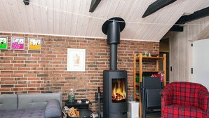 Ein gemütliches Wohnzimmer mit Backsteinwand, Kamin, grauem Sofa, rotem Karosessel und Holzbalkendecke.