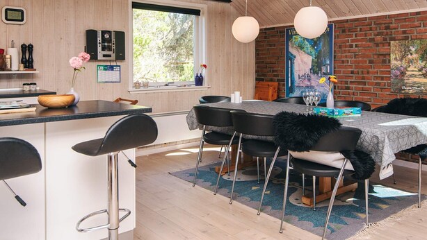 A modern dining area with a wooden ceiling, black chairs, a central table with a white tablecloth, and hanging pendant lights.