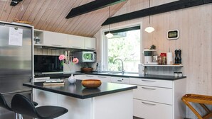 Eine moderne Küche mit einer zentralen Kochinsel, Barhocker, einer Holzbank und Blick ins Freie.