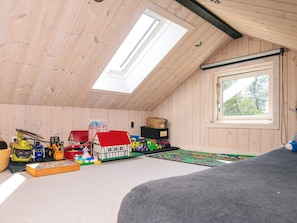 A room with wooden walls and a sloped ceiling, featuring skylights, a large window, and a play area with toys and a play mat. - 4 Star Holiday Home in Blavand (Blavand)