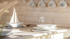 A wooden dining table with white plates, a glass, and a decorative sailboat centerpiece. - Houseboat Grey Seal Comfortable Vacation Home (Heiligenhafen)