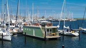 A marina with numerous sailboats docked, a green floating structure with a deck and windows, and a clear blue sky. - Houseboat Grey Seal Comfortable Vacation Home (Heiligenhafen)