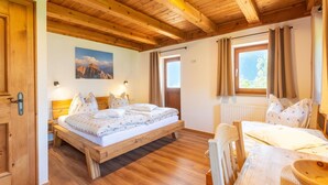 A wooden-floored bedroom with a large bed, two bedside tables, and a window with curtains. - Renovated Farmhouse Stoanerbauer With View (Bramberg am Wildkogel)