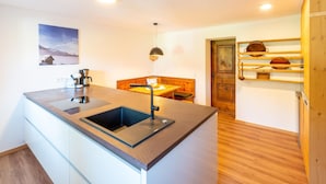 A modern kitchen with a central island, wooden bench seating, and a wooden door with shelves. - Renovated Farmhouse Stoanerbauer With View (Bramberg am Wildkogel)