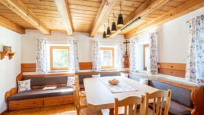 A cozy room with wooden beams, a dining table with chairs, a bench, and a window with floral curtains. - Renovated Farmhouse Stoanerbauer With View (Bramberg am Wildkogel)