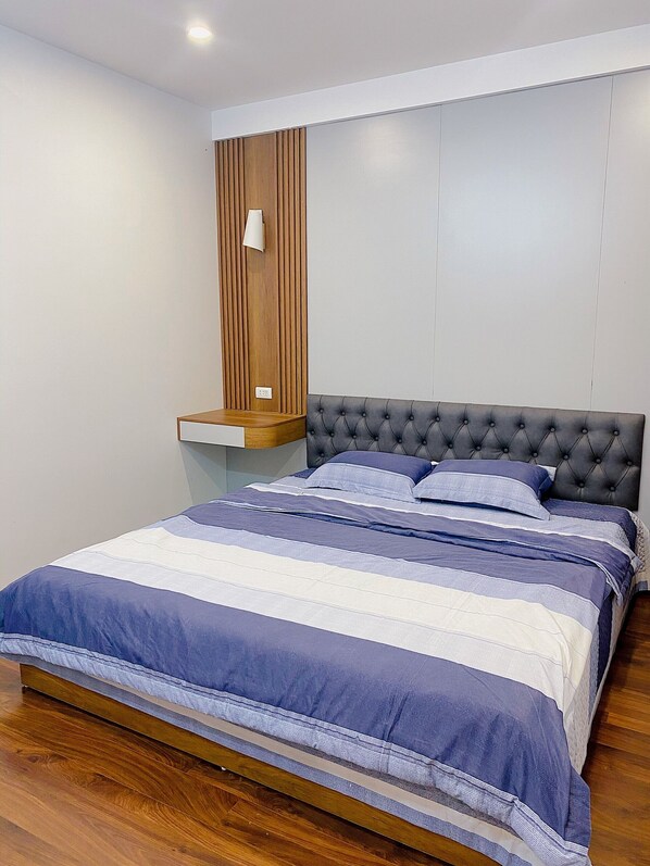 Un dormitorio moderno con un cabecero capitonado, una pared de acento de madera y una colcha a rayas.