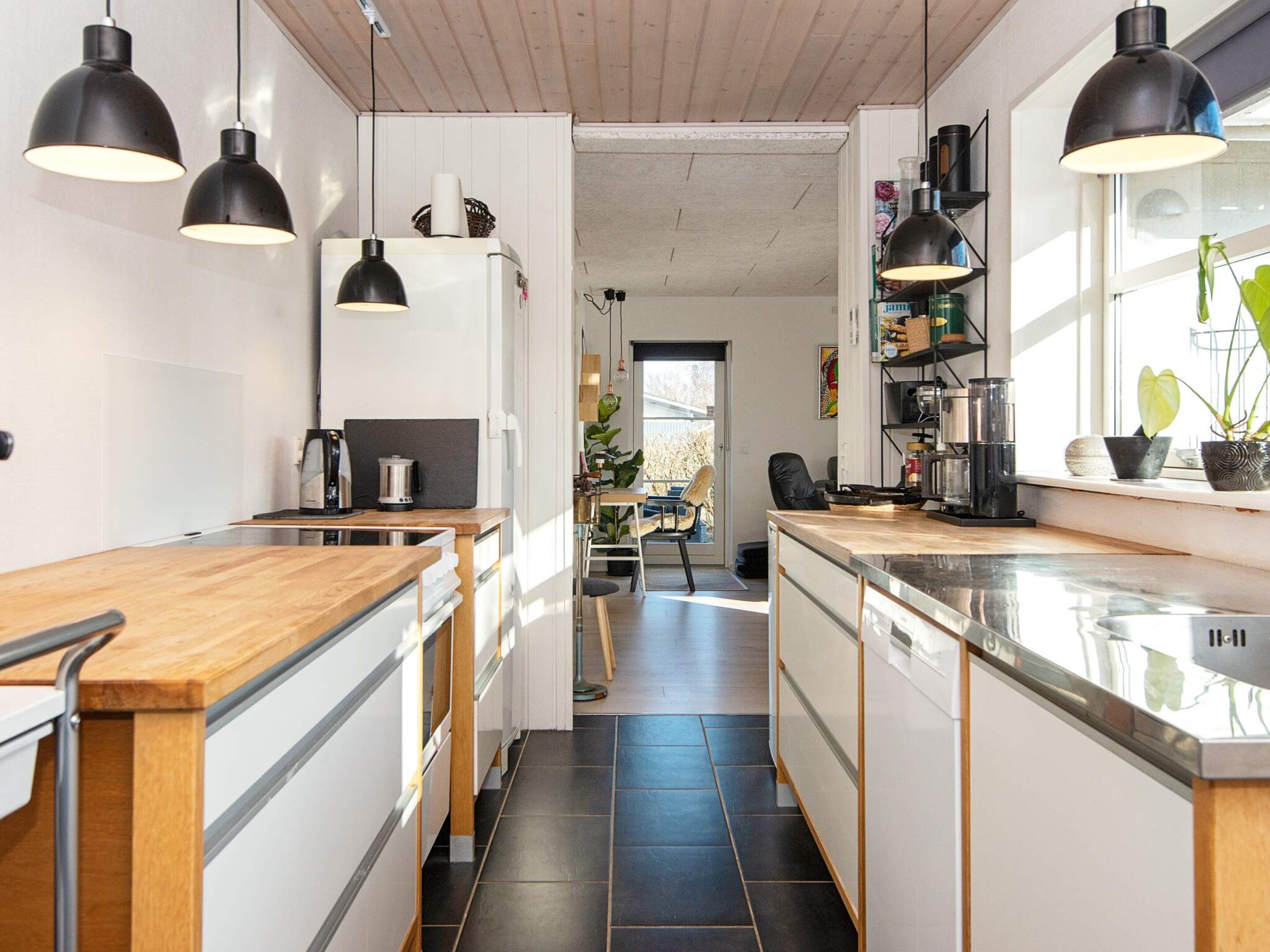 A modern kitchen with wooden countertops, black pendant lights, and a view into the dining area.