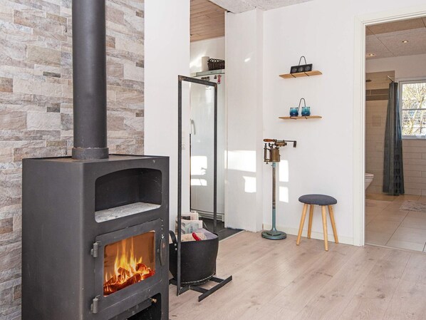 A modern living room with a stone wall, a black wood-burning stove, a mirror, and a small stool.