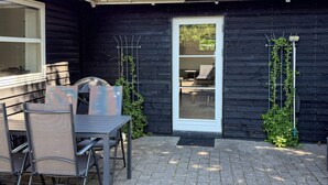 A patio with a table and chairs, a door, and a small garden area with climbing plants. - 4 Person Holiday Home in Ebeltoft (Ebeltoft)