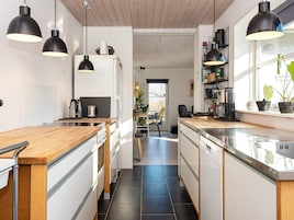 A modern kitchen with wooden countertops, black pendant lights, and a view into the dining area.