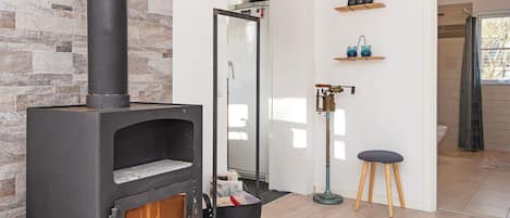 A modern interior with a stone wall, a wood-burning stove, a mirror, and a small stool.