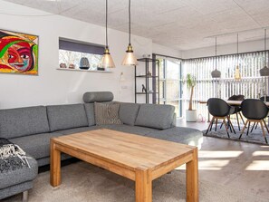 A modern living room with a grey sofa, a wooden coffee table, and a dining area with a table and chairs. - 4 Person Holiday Home in Ebeltoft (Ebeltoft)