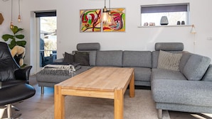 A modern living room with a grey sectional sofa, a wooden coffee table, and a colorful abstract painting. - 4 Person Holiday Home in Ebeltoft (Ebeltoft)