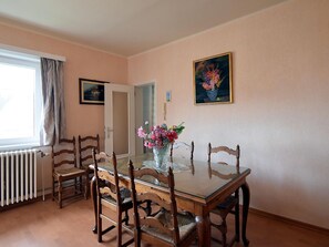 A dining area with a glass-top table, wooden chairs, a vase with flowers, and a painting on the wall. - Cocktail 0101 Apartment in De Haan With Terrace (De Haan)