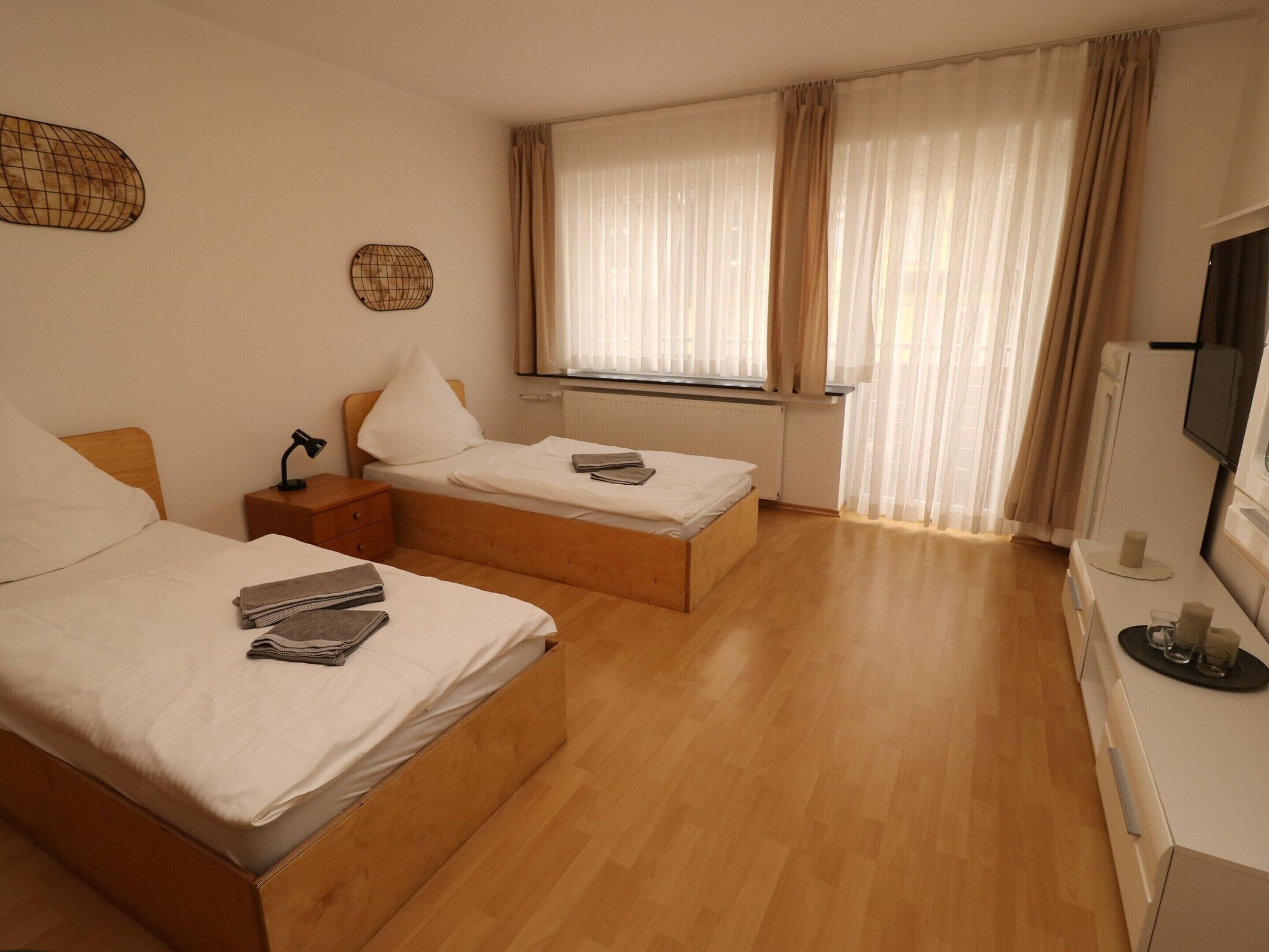 Una camera d'albergo con due letti, pavimento in legno, televisione e finestra con tende.