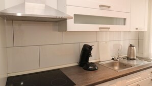 Eine moderne Küche mit weißen Schränken, einer Edelstahl-Dunstabzugshaube, einem schwarzen Induktionskochfeld, einem Wasserkocher und einer Kaffeemaschine.