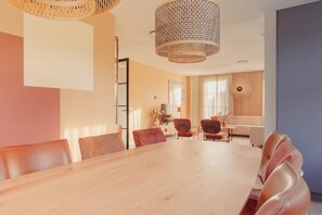 A modern dining area with a wooden table and leather chairs, a woven ceiling light fixture, and a view of a living room with a sofa and a window. - Villa With Jacuzzi and Sauna in Makkum (Makkum)