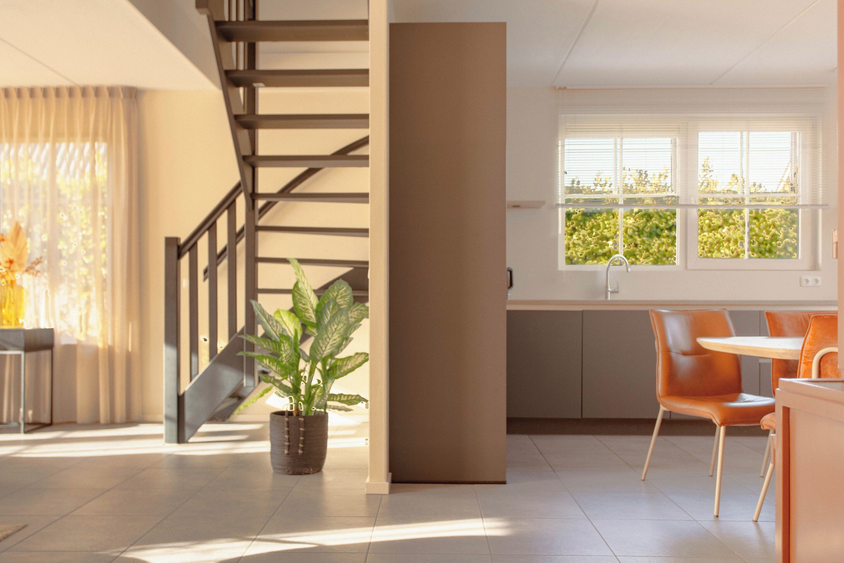 A modern interior with a staircase, a dining area with chairs, and a window with blinds.