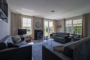 A living room with a fireplace, two sofas, a television, and a clock on the wall. - Villa With Whirlpool and Sauna in Makkum (Makkum)