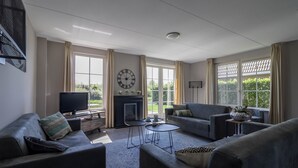 A living room with a fireplace, two sofas, a TV, and a clock on the wall. - Villa With Jacuzzi and Sauna in Makkum (Makkum)
