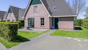 A row of brick houses with pitched roofs, a paved walkway, and a small green area with a bench. - Villa With Jacuzzi and Sauna in Makkum (Makkum)