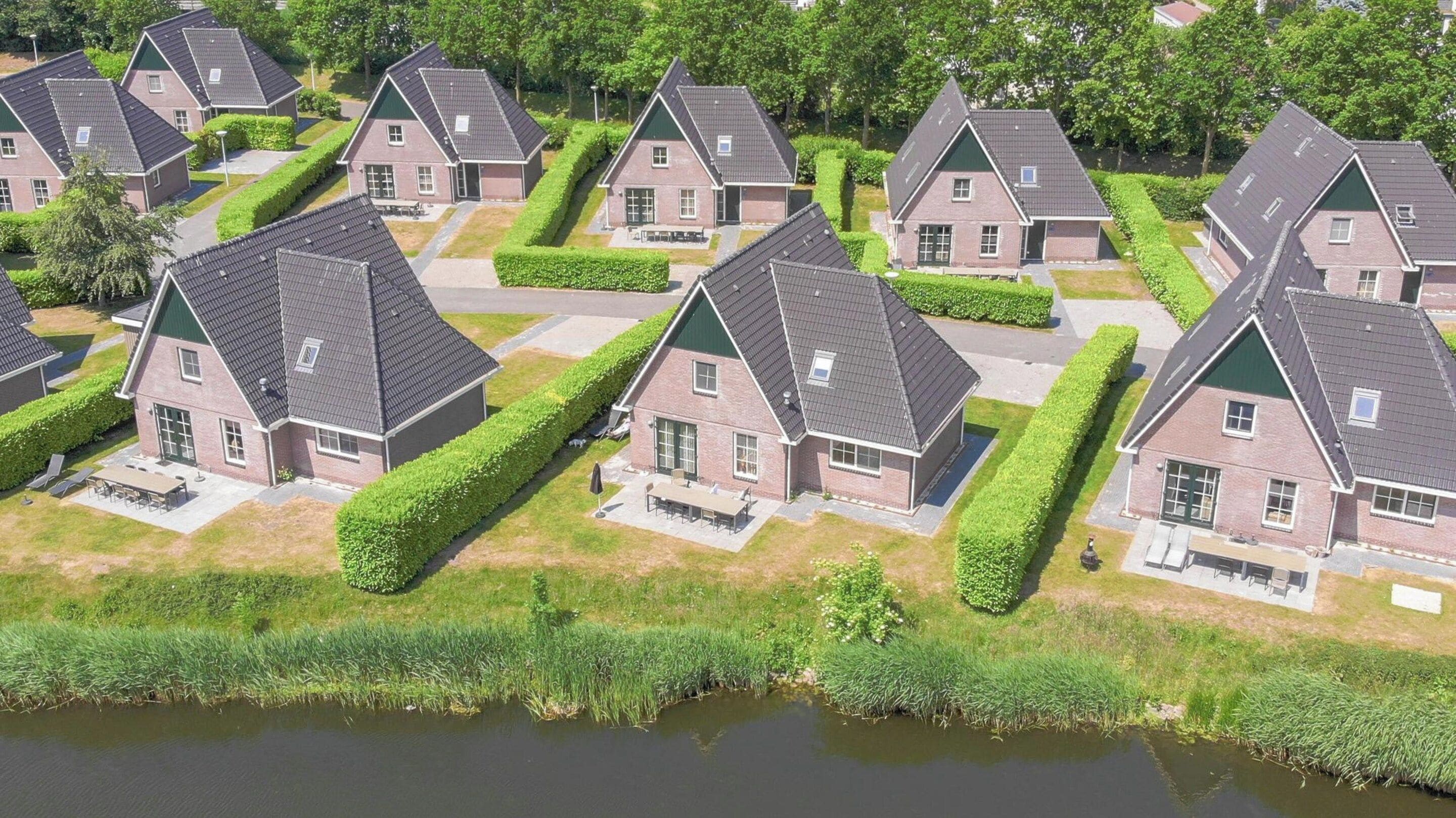 A residential area with multiple houses featuring pitched roofs and brick exteriors, arranged in a grid pattern with a body of water in the foreground.