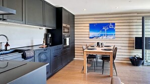 A modern kitchen with dark cabinets, a dining area with a wooden table and chairs, and a large window with a view of a ski lift.