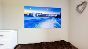 A bedroom with a bed, a white dresser, and a framed picture of a snowy landscape on the wall.