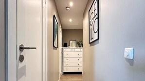 A narrow hallway with a wooden floor, a white door, and a white dresser with drawers.