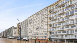 Un edificio residencial de varios pisos con balcones, pavimento mojado y automóviles estacionados.